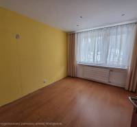 Ein Zimmer mit gelber Wand, einem Fenster mit zarten Vorhängen und einem Boden mit Holzdekor.