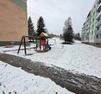 Kinder spielen auf einem verschneiten Spielplatz vor Plattenbauten in Považská Bystrica, 4-Zimmer-Wohnung.
