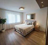 Schlafzimmer mit Bett, Spiegel und Nachttischen in einer 4-Zimmer-Wohnung mit Holzboden.