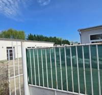 Weißes Gebäude in Šaľa, Teil von Lagern und Hallen, umgeben von einem Zaun und Grünflächen.