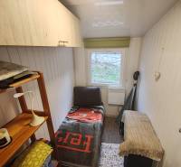 Ein kleines Zimmer in der Hütte mit einem Bett, einem Regal und einem Fenster, Holzmöbeln und Holzwänden.