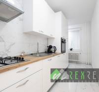 Küche mit weißen Schränken, Marmorboden und eingebauten Geräten in einer 3-Zimmer-Wohnung.