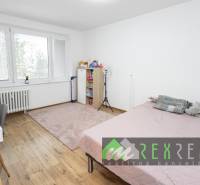Schlafzimmer in einer 3-Zimmer-Wohnung mit Bett, Tisch, Regalen und Boden mit Holzdekor.