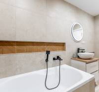 Badezimmer in einer 2-Zimmer-Wohnung mit Badewanne, Waschbecken und Spiegel mit Holzdekor.