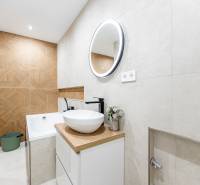 Badezimmer einer Zweizimmerwohnung mit hellen Fliesen und einem Boden in Holzoptik.