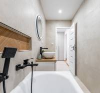 Badezimmer in einer 2-Zimmer-Wohnung mit Badewanne, Waschbecken und rundem Spiegel.