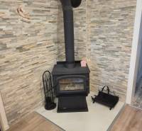 Ein Kamin für Holz in der Ecke des Raumes mit Steinverkleidung und einem Boden in Holzoptik.