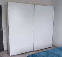 Ein weißer Schrank und ein Bett mit einer blauen Decke im Inneren eines Einfamilienhauses.