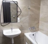 Badezimmer mit Badewanne, Waschbecken und Spiegel, mit Fliesen in Sandtönen.