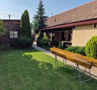 Ein Einfamilienhaus in Dlhá nad Váhom mit Rasen, Sträuchern und einer Holzbank im Garten.