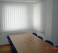 Gewerbeflächen mit Konferenztisch, blauen Stühlen und vertikalen Jalousien.