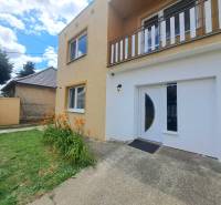 Ein Einfamilienhaus in Veľká Mača mit orangefarbenen Blumen, grünem Rasen und Eingangstüren.