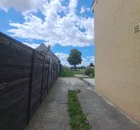Ein Einfamilienhaus in Veľká Mača neben einem Holzzaun, eine Betonstraße, Wolken und ein Baum.