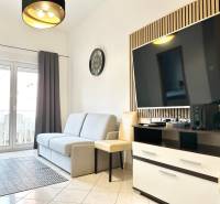 Wohnzimmer mit Sofa und Fernseher in einer Ferienwohnung, heller Fliesenboden, Balkontüren.