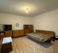 Schlafzimmer mit Möbeln im Retro-Stil, Boden mit Holzdekor, großes Fenster mit Heizkörper.