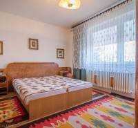 Schlafzimmer in einem Einfamilienhaus mit Bett, Teppichen und Vorhängen am Fenster.