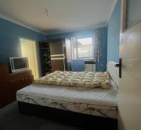 Ein Schlafzimmer mit einem Bett, einem dunklen Kleiderschrank, einem Fernseher und blauen Wänden in einem Einfamilienhaus.