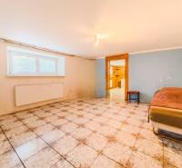 Ein Zimmer mit Fliesen in einem Einfamilienhaus, ein Bett an der Wand, ein Fenster mit Heizkörper.