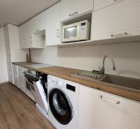 Küche in einer Einzimmerwohnung mit weißer Küchenzeile, Waschmaschine und Boden in Holzoptik.