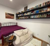 Einzimmerwohnung mit Bibliothek, Kunst an der Wand und einem Bett mit purpurner Tagesdecke.