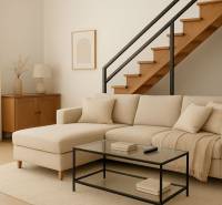 Innenraum eines Gebäudes mit einem beigen Sofa, einer Treppe und einem Boden in Holzoptik.