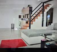 Wohnzimmer mit Küchenzeile, Treppe, Sofa, Glastisch und Holzboden.