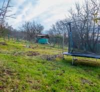 Trampolin und Gartenhaus in einem Garten in Prešov, umgeben von Bäumen und Gras.