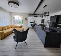 Wohnzimmer mit großem Sofa und moderner Küche, Boden mit Holzdekor.