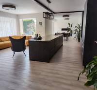 Küche und Wohnzimmer im Einfamilienhaus mit Insel, gelbem Sofa und Boden in Holzoptik.