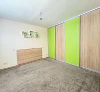 Ein Zimmer in einer 3-Zimmer-Wohnung mit Teppichboden und einem eingebauten Schrank mit grünen Schiebetüren.