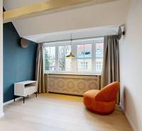 Ein Zimmer in einer 4-Zimmer-Wohnung mit einem orangefarbenen Sessel, einem hellen Boden in Holzoptik und einem großen Fenster.