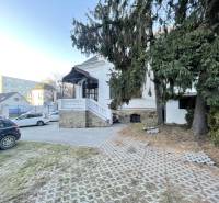 Das Gebäude in der Vajanského-Straße in Prešov mit Zufahrtsstraße, Autos und Tannen im Vordergrund.