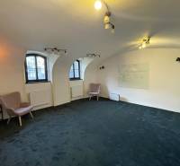 Interieur eines Gebäudes mit Bogenfenstern, grünem Teppichboden und Wandtafel.