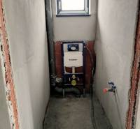 Vorbereitung für die Installation einer Toilette im Einfamilienhaus mit eingebautem Spülkasten, weißen Wänden und kleinem Fenster.