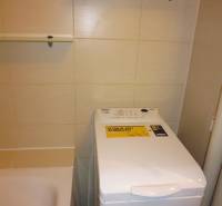 Badezimmer in einer 2-Zimmer-Wohnung mit Waschmaschine neben der Badewanne und Regalen.