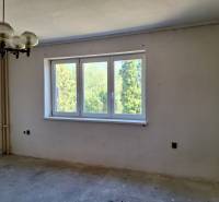 Ein Zimmer in einem Einfamilienhaus mit einem großen Fenster, einem originalen Kronleuchter und Blick ins Grüne.