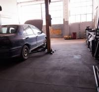 Ein Auto auf einem Hebebühne im Inneren eines Produktionsbereichs mit großen Fenstern.