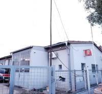 Produktionsräume in der Stadt Veľké Úľany mit grauer Fassade und einem roten Auto hinter dem Zaun.