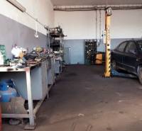 In der Werkstatt gibt es Werkzeuge, ein Auto auf dem Hebebühne und verstreute Teile auf dem Boden.