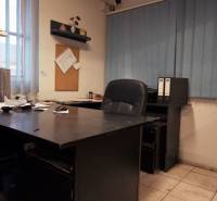 Ein Büro mit einem dunklen Tisch, Fliesenboden und blauen vertikalen Jalousien in einem Produktionsbereich.