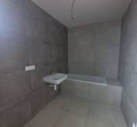 Badezimmer mit großformatigen grauen Fliesen, Waschbecken und Badewanne in einem Einfamilienhaus.