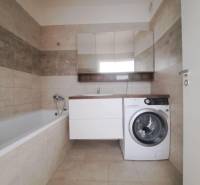 Badezimmer in einer 2-Zimmer-Wohnung mit Badewanne, Waschmaschine und beigen Fliesen.