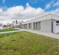 An der Vajanského-Straße befinden sich Geschäftsräume, neben dem Gehweg ist eine grüne Rasenfläche.