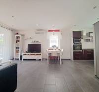 Wohnzimmer mit Fernseher, Küche und Esstisch, Boden mit Holzdekor.