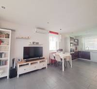 Wohnzimmer in einem Einfamilienhaus mit Fernseher, Kochnische und einem Tisch mit drei Stühlen.