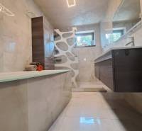 Ein Badezimmer in einem Einfamilienhaus mit Badewanne, moderner Beleuchtung, Fliesen und Waschbecken.