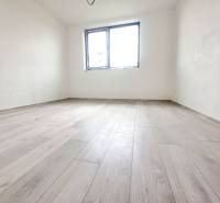 Ein Zimmer in einem Einfamilienhaus mit einem Boden in Holzoptik, weißen Wänden, einem Fenster.