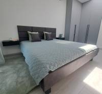 Schlafzimmer mit großem Bett, grauen Schränken und schwarzem Kronleuchter in einer 2-Zimmer-Wohnung.