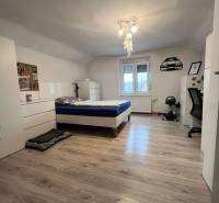 Ein Schlafzimmer in einem Einfamilienhaus mit einem Bett, weißen Möbeln und einem Boden in Holzoptik.