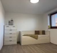 Ein Zimmer in einem Einfamilienhaus mit einem Bett, einer Kommode und einem Boden in Holzoptik.